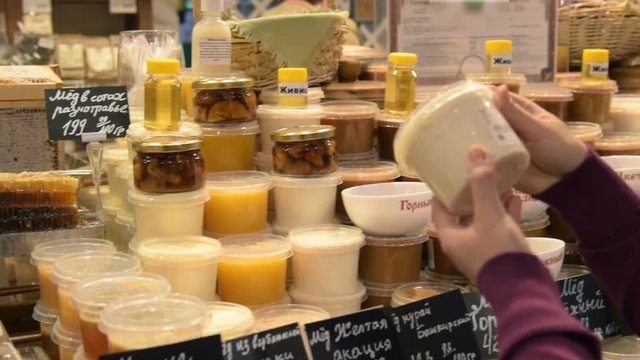 Woman looking over the plastic jars with different kinds of honey. Great assortment of natural product