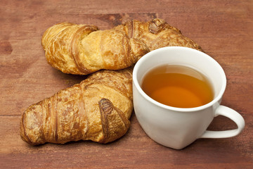 Cup of tea with two appetizing croissants, on wooden texture