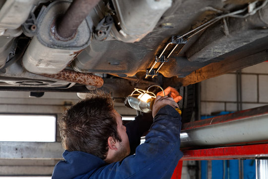 auto mechanic checks the bottom of a car under platform