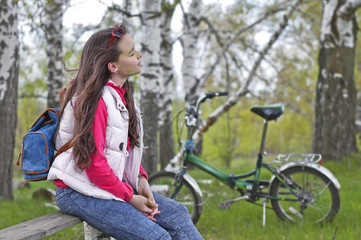 Fototapeta na wymiar Girl resting in the spring forest sitting on a bench