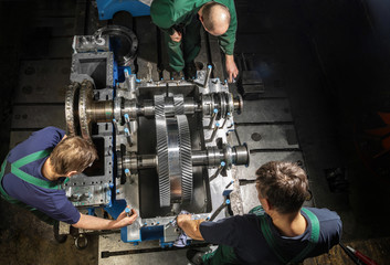 Working people with a small steam turbine. Metal gears. Gear wheels of the engine.