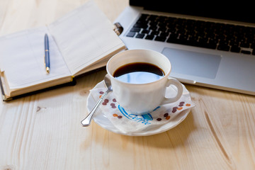 Coffee cup notepad, and laptop on wood table.