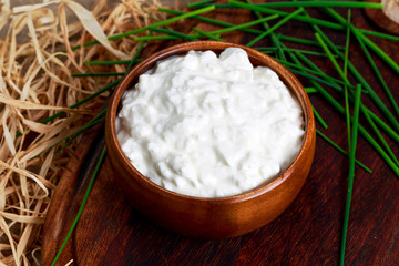 Cottage cheese with chives in wooden bowl on straw. 