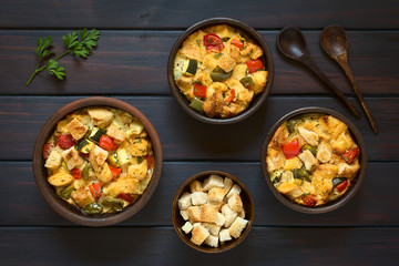 Herzhafter Brotpudding mit Gemüse (Zucchini, Paprika, Tomate) in rustikale Schüsseln, fotografiert auf dunklem Holz mit natürlichem Licht 