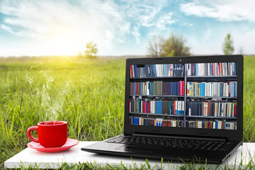 Laptop and cup of hot coffee on the background picturesque nature, outdoor office. E-book library...