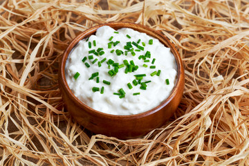 Cottage cheese with chives in wooden bowl on straw. 