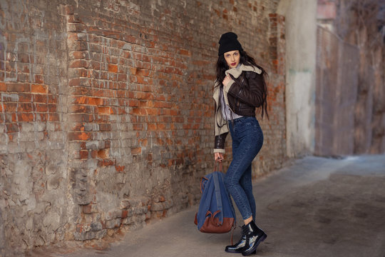 Outdoor lifestyle portrait of pretty young girl, wearing hipster swag grunge style on urban background. Wearing hat and jeans with backpack. Spring fashion woman. Toned style instagram filters.