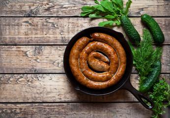 Plakat Traditional homemade spicy baked meat sausage with cucumber and herbs in cast iron pan on vintage wooden table background