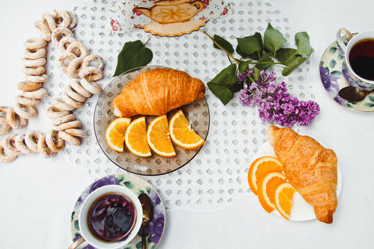 Beautiful and healthy Breakfast: croissants and coffee on the table with oranges and lilac flowers