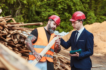 Director the suit and helmet and worker in overalls and with a tattoo are checking the quality of materials and other inspections