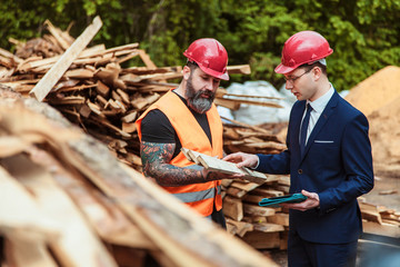 Director the suit and helmet and worker in overalls and with a tattoo are checking the quality of materials and other inspections