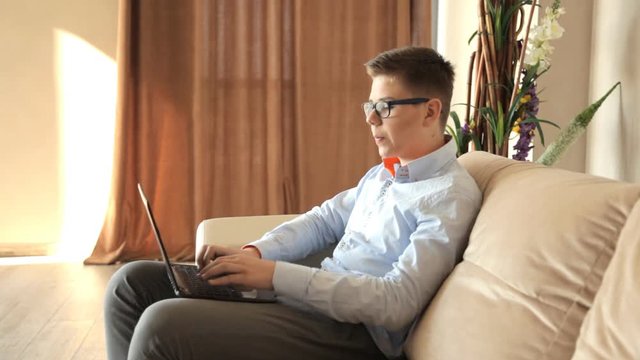 Мальчик работает за ноутбуком сидя на диване