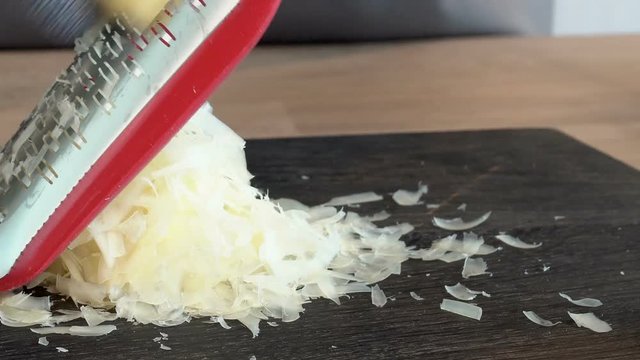 cook glove rubs cheese on grater on cutting board