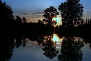 Sunset over dead arm (cove) of the river sluice surrounded by trees.