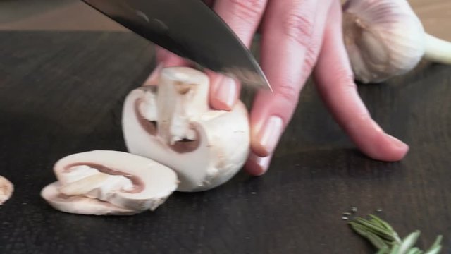cook cuts mushrooms with a sharp knife on a cutting board