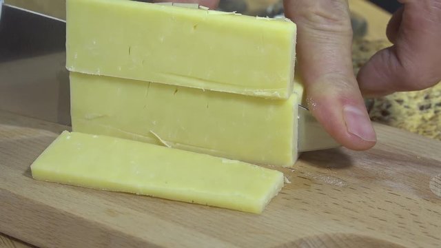 Slicing white cheddar cheese on a cutting board
