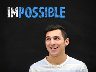 Young man near blackboard with word impossible transformed into possible