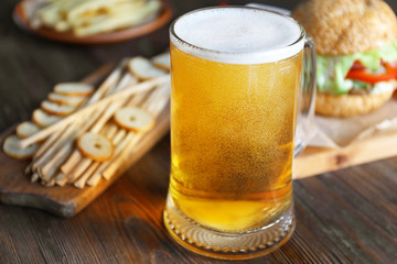 Glass mug of light beer with snacks on dark wooden table, close up