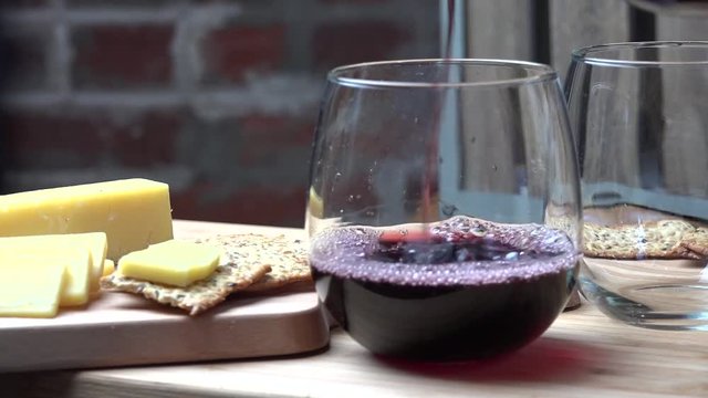 Pouring red wine into a glass with cheese and crackers
