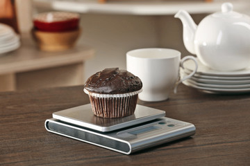 Chocolate cupcake and digital kitchen scales on wooden table
