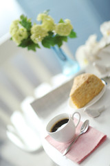 Cup of coffee with cake on white table in light interior