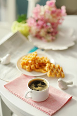 Cup of coffee with wafers on white table in light interior