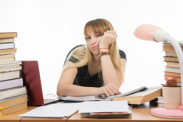 Student sadly sitting at a table among the stacks of books and papers