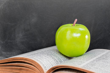 Green apple on old  open book over black chalkboard background