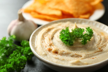Ceramic bowl of tasty hummus with chips and parsley on table