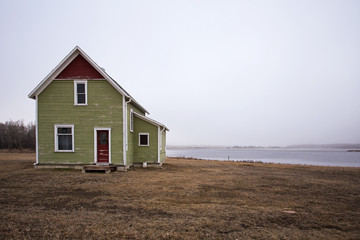 Obraz premium Old two storey green and red abandoned house in front of a fog shrouded lake in countryside landscape