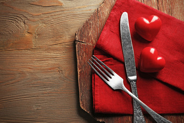 Composition of fork, knife, napkin and decorative hearts on cutting board, on wooden table...