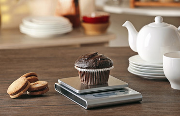 Chocolate cupcake and digital kitchen scales on wooden table