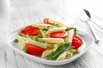 Boiled penne pasta with tomatoes, French bean and arugula on white plate