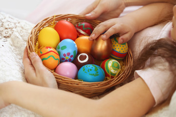 Fototapeta na wymiar Mother and daughter hands holding wicker basket with colorful Easter eggs closeup