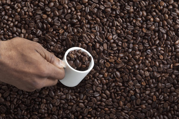 hand holding cup of coffee beans over pile