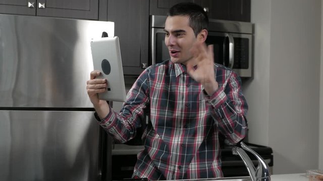 Young man in a home kitchen using a tablet to video chat (facetime).