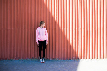 beautiful girl in a pink sports hoodie standing near the wall in the shade