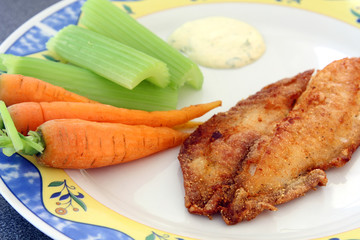 decorated plate with fried fish: river trout filet with carrots, celery and sauce, served