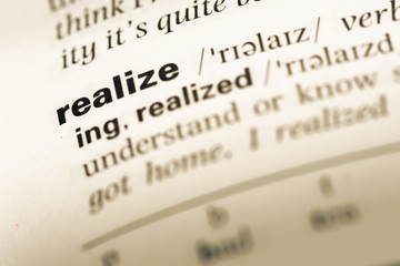 Close up of old English dictionary page with word realize - obrazy, fototapety, plakaty