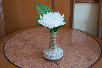 White flower with green leaf in bouquet put in ceramic vase on brown wooden table/White flower in vase on wooden table