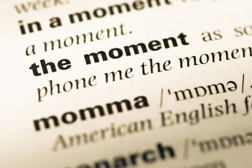 Obraz premium Close up of old English dictionary page with word the moment