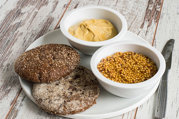 Mustard and bread.  Mustard and rye bread on a dish on a light wooden background.