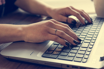 Side view of woman's hands writing on laptop.