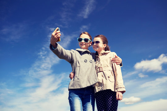 happy girls with smartphone taking selfie outdoors