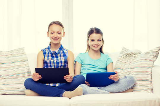 happy girls with tablet pc sitting on sofa at home