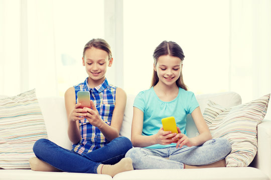 happy girls with smartphones sitting on sofa