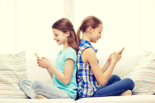 happy girls with smartphones sitting on sofa