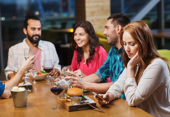 woman with smartphone and friends at restaurant