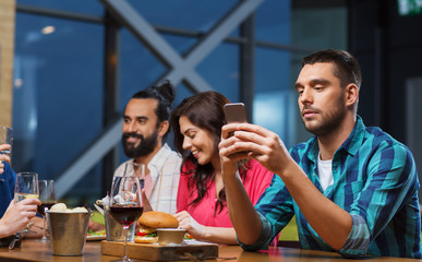 man with smartphone and friends at restaurant - Powered by Adobe