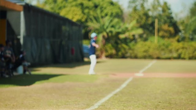 Slow motion of boy batting at baseball game and runner on third base